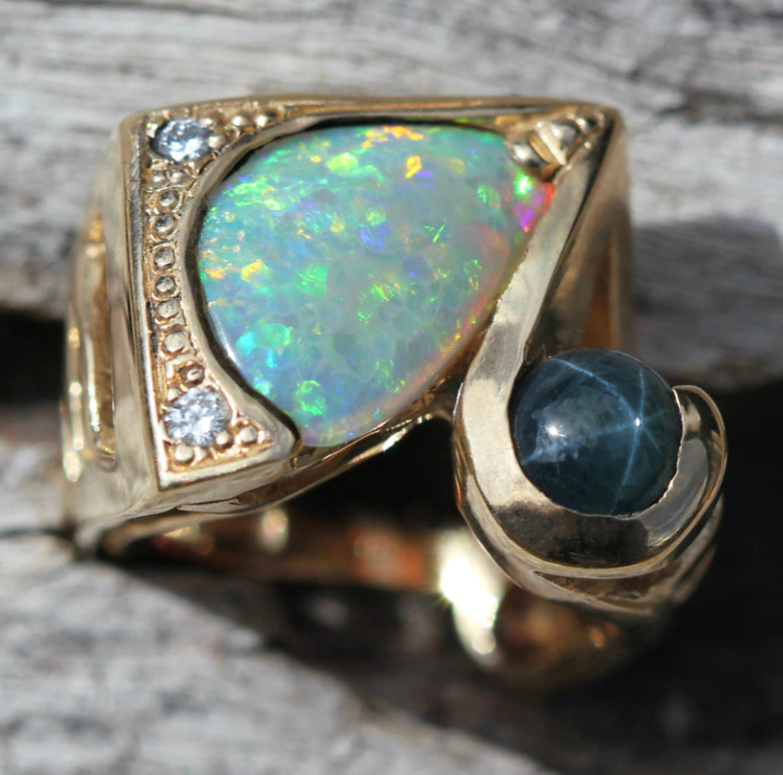 Angled macro highlighting the opal play-of-color, the dark blue star sapphire cabochon and textured gold gallery.