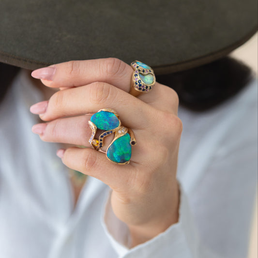 Styled hand shot showing the 5.85ct Lightning Ridge opal, sapphire and diamond cocktail ring in 18ct yellow gold worn on the index finger.