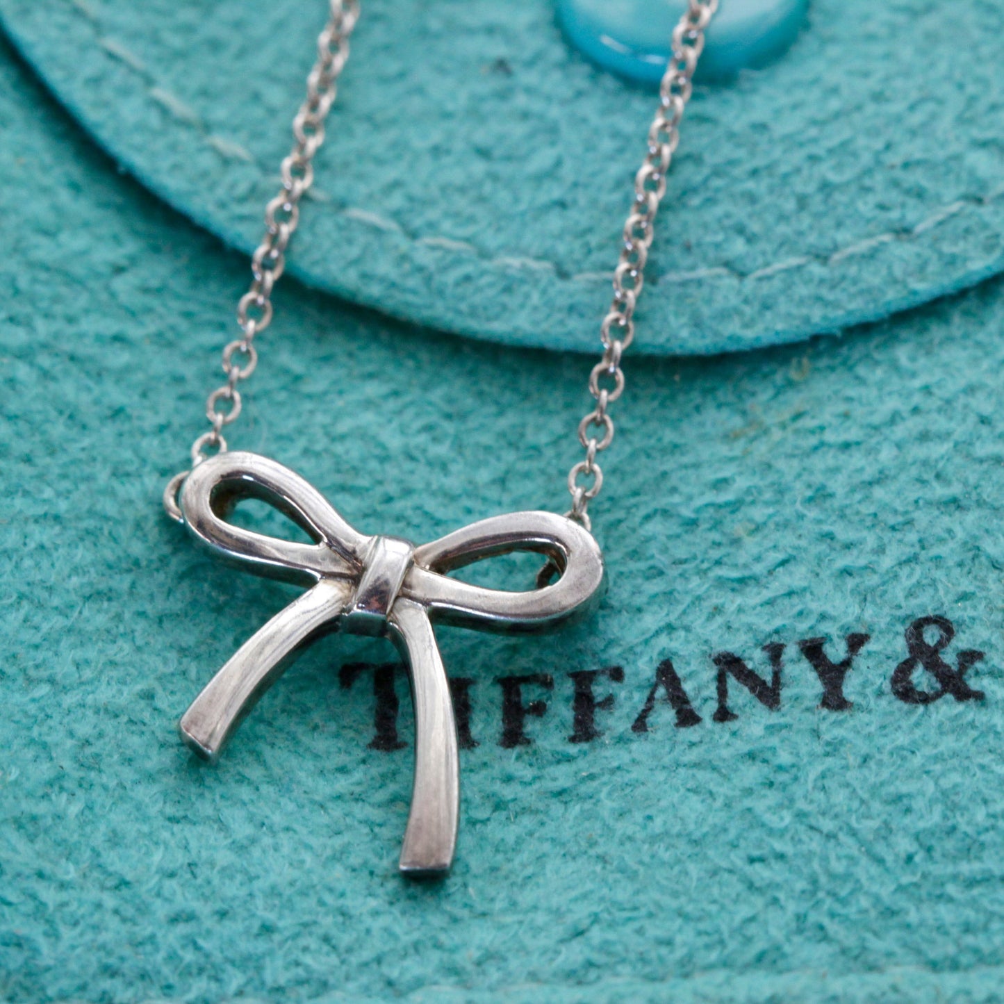 Close-up of vintage Tiffany & Co. Elsa Peretti Bow sterling-silver pendant and chain on Tiffany blue pouch