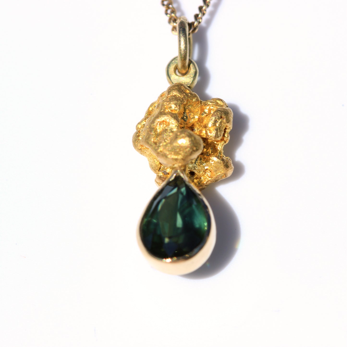 Close-up of an Australian parti sapphire teardrop set beneath a natural gold nugget pendant on a white background.