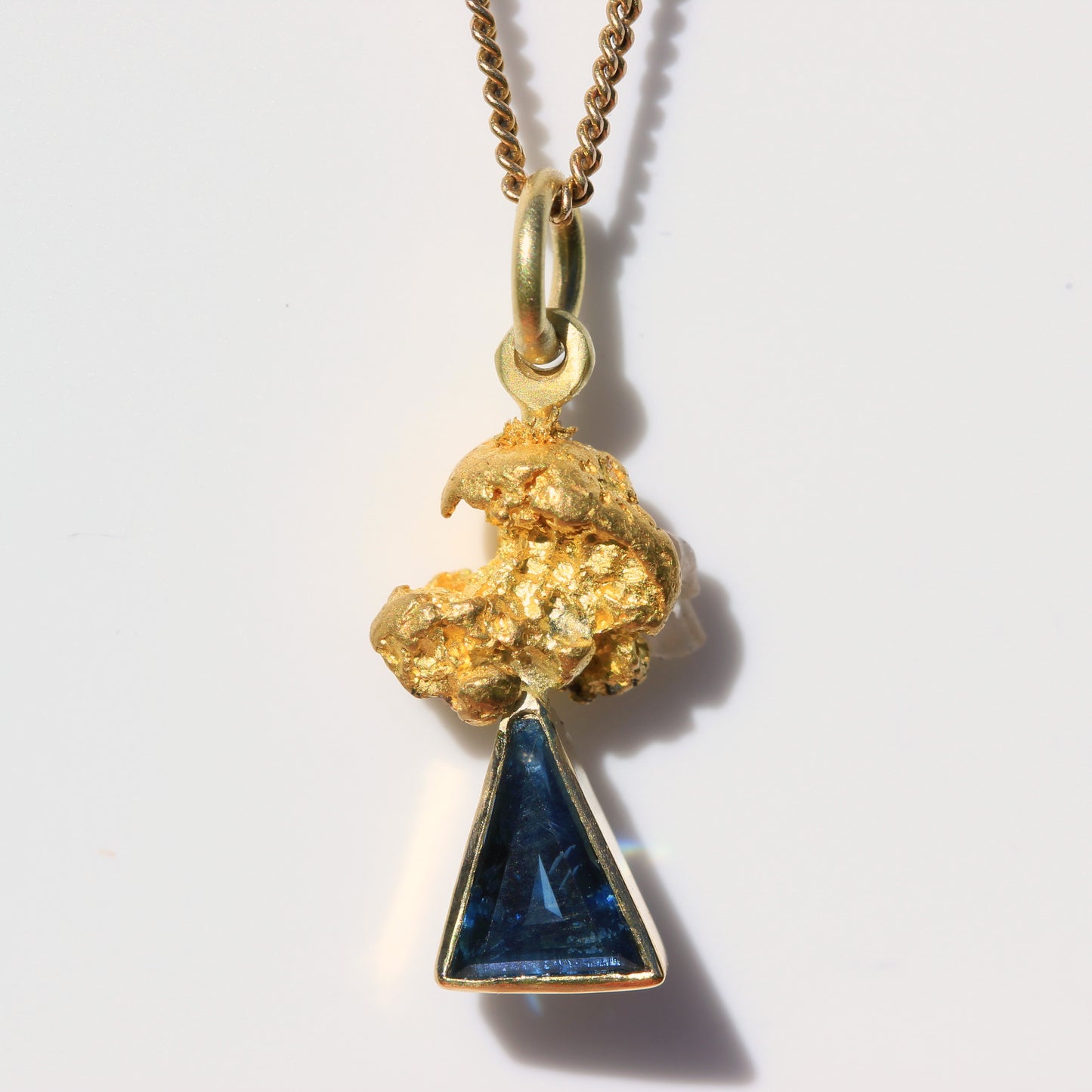 Close-up of an Australian parti sapphire triangle pendant set below a natural gold nugget (92–98% pure gold) on a chain.