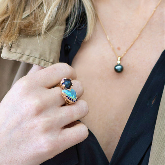 Woman wearing Lightning Ridge opal and Tahitian pearl ring with blue sapphire accents in 14ct yellow gold on right hand