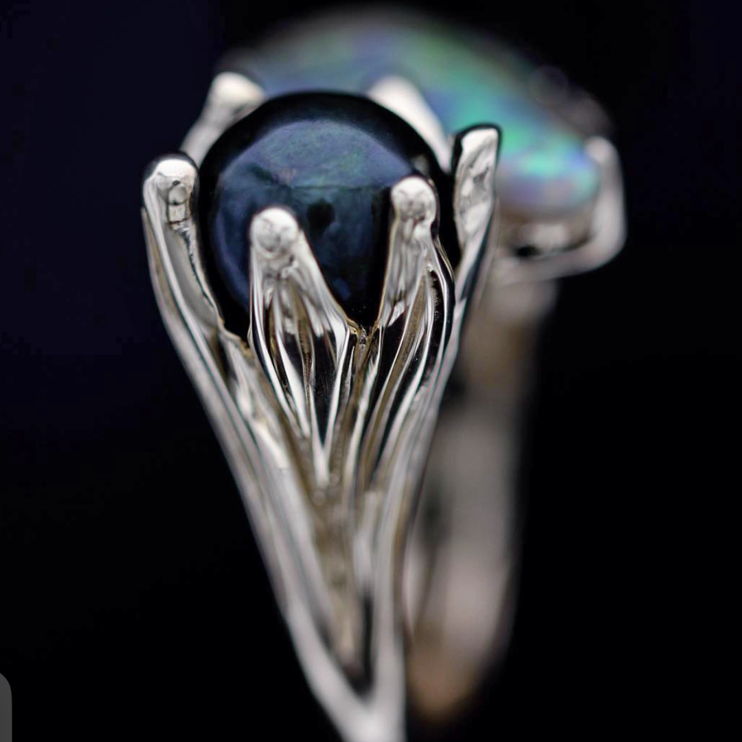 Close-up of Tahitian South Sea pearl held in sculptural claw setting on 14ct yellow gold ring with Lightning Ridge opal
