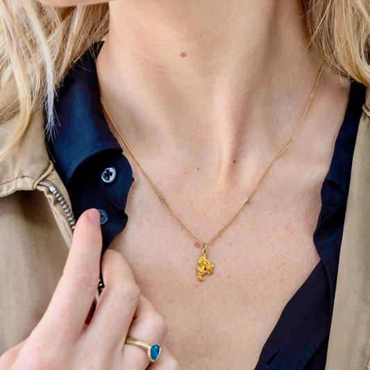 Natural gold nugget pendant on fine chain, shown on woman's neck against a dark blouse.