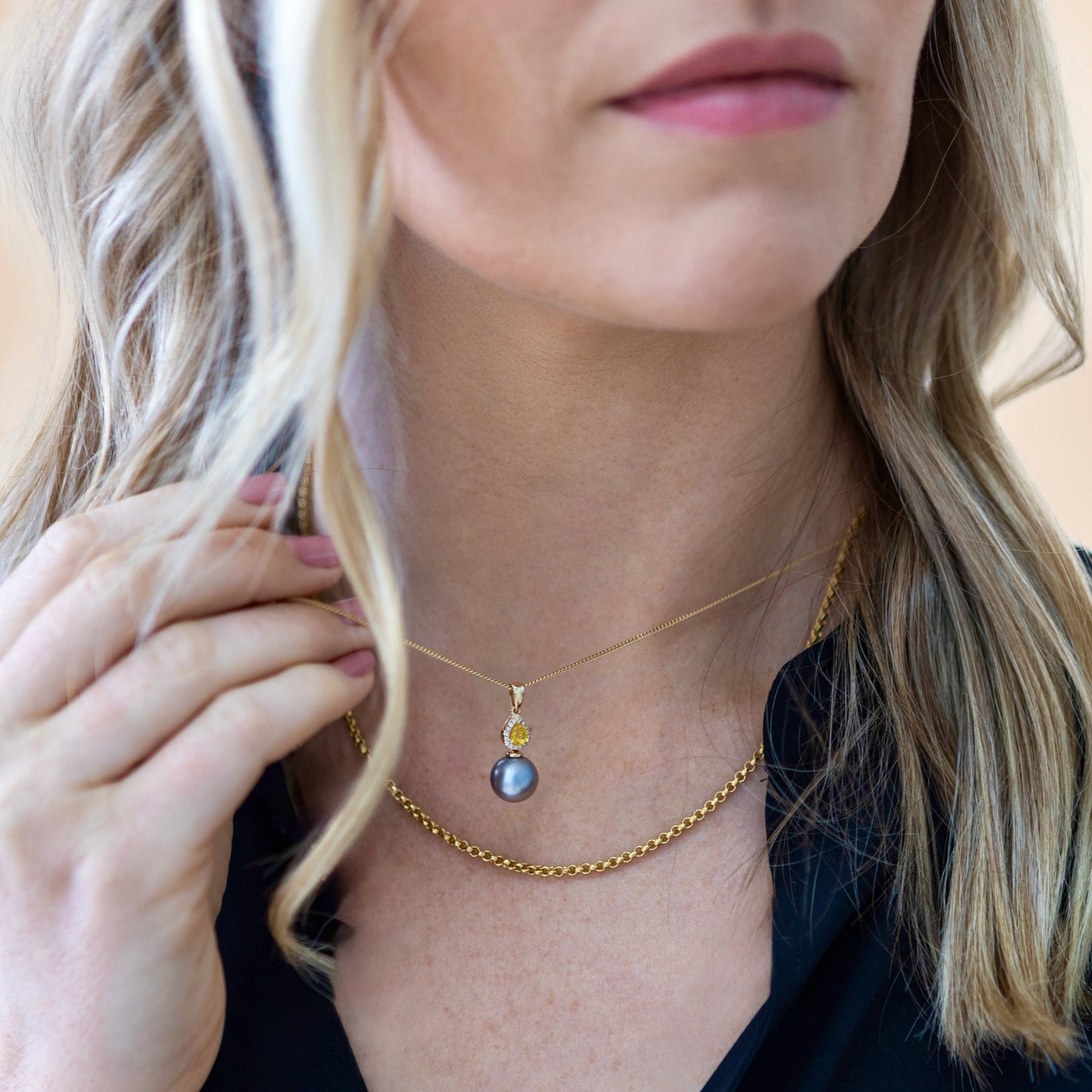 Angled macro of 14ct yellow gold pendant highlighting Tahitian pearl luster and sparkling diamond halo around yellow sapphire.