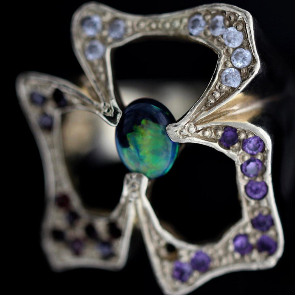 Close-up of the black opal cabochon and pavé garnet and sapphire accents on the 14ct yellow gold statement ring.