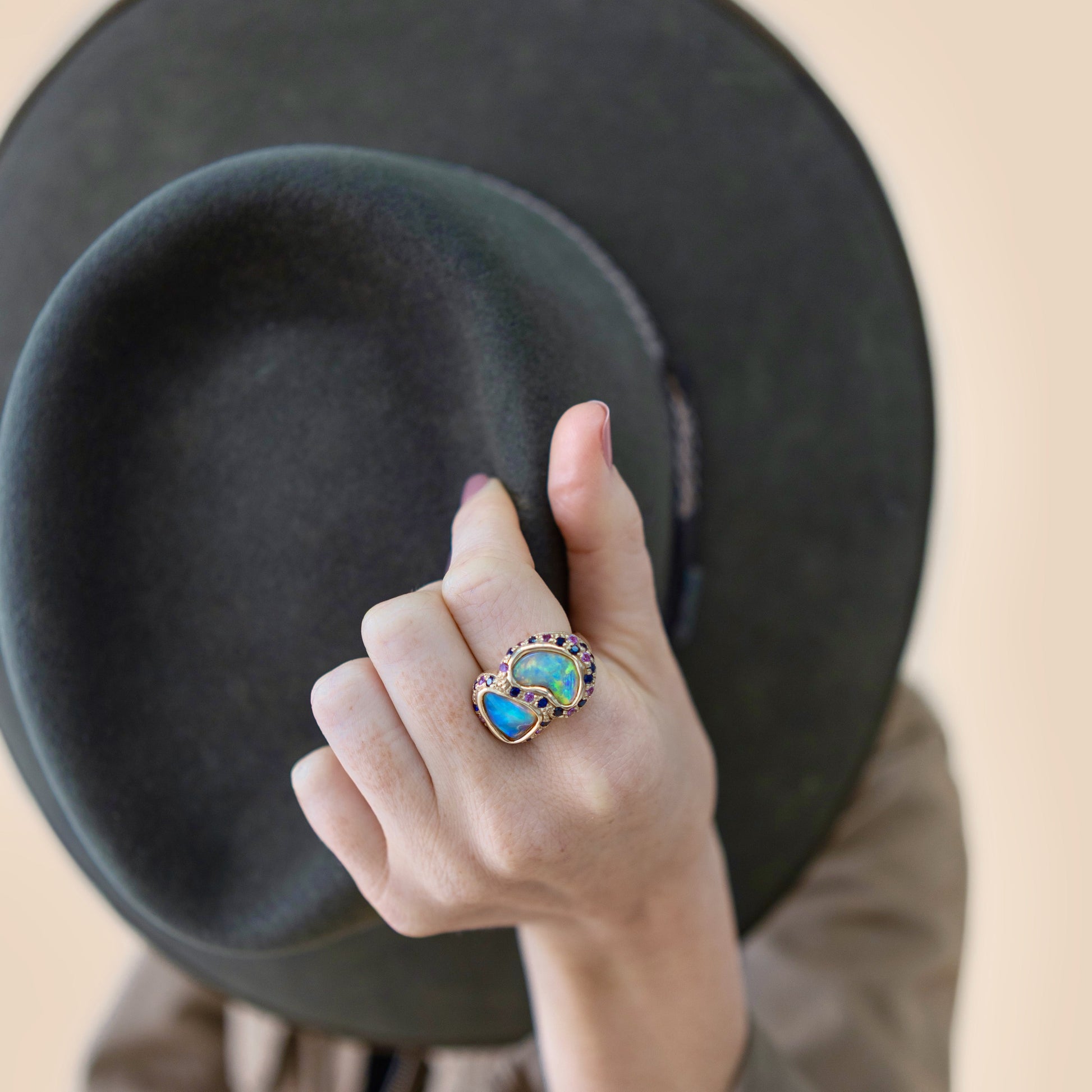 Lifestyle shot of the double opal and sapphire cluster ring on a finger, 14ct yellow gold setting.