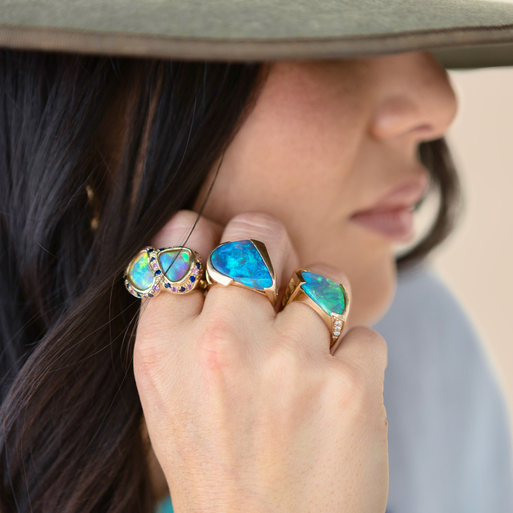 Ring worn on hand, showing two bezel-set opals with blue and purple sapphire accents in a curved cluster design.