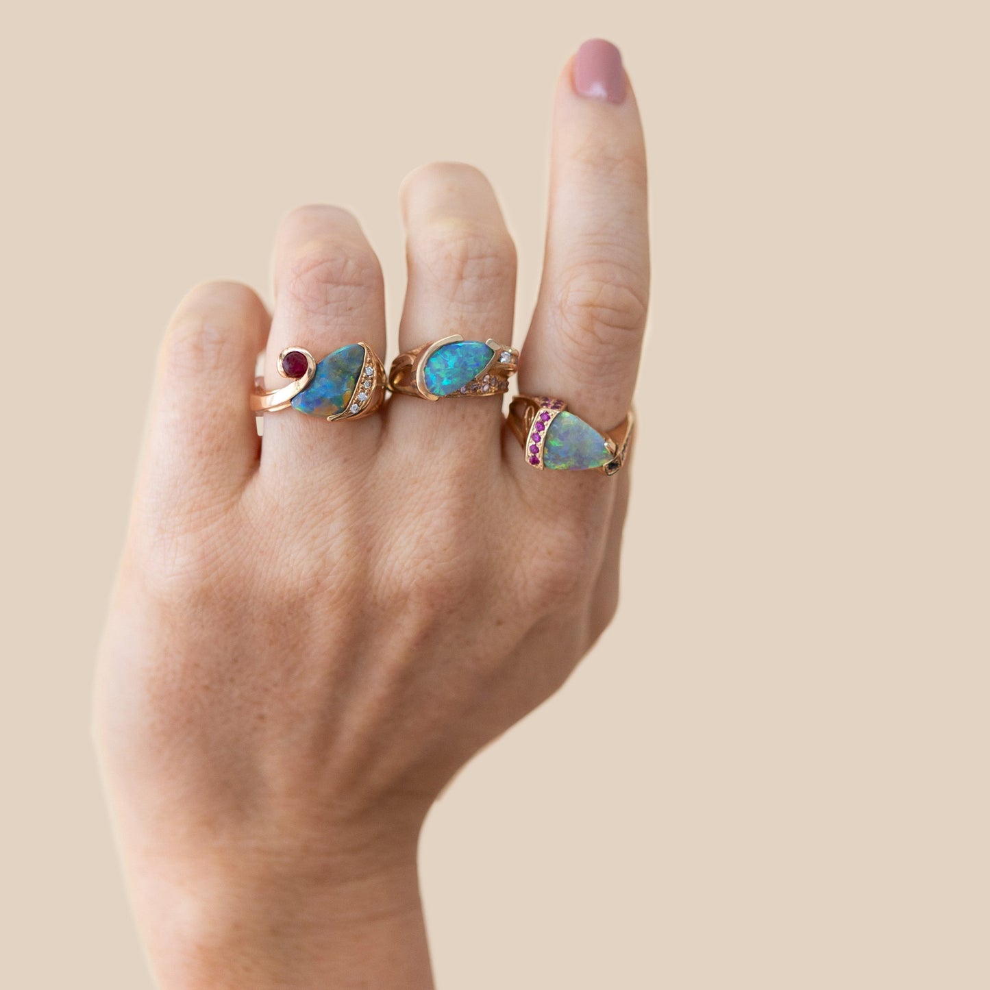 Model wearing the pear-cut Lightning Ridge opal, diamond and pink sapphire ring in 14ct yellow gold, stacked with two other opal rings.