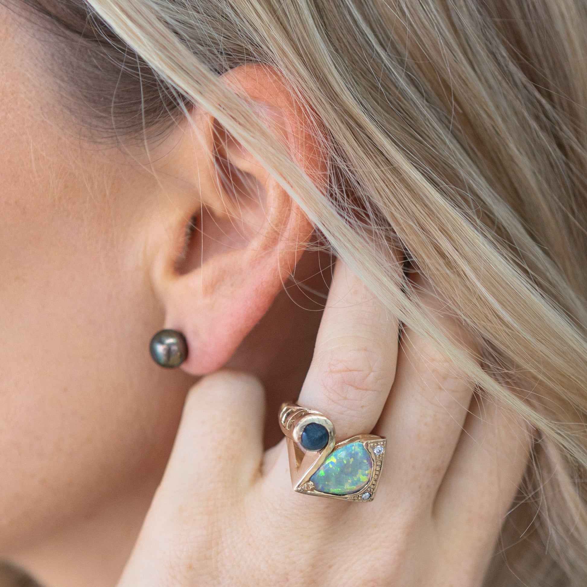 Close-up of ear wearing a 10mm black Tahitian pearl stud earring in 14ct yellow gold; lifestyle view for scale.