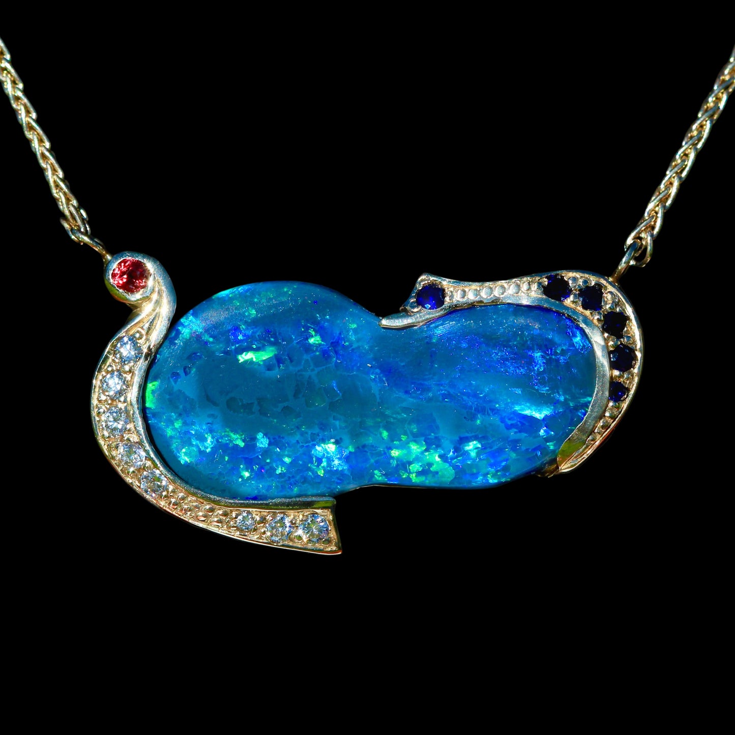 Close-up of vivid blue-green Lightning Ridge opal framed by sapphire and diamond accents in 14ct yellow gold necklace.