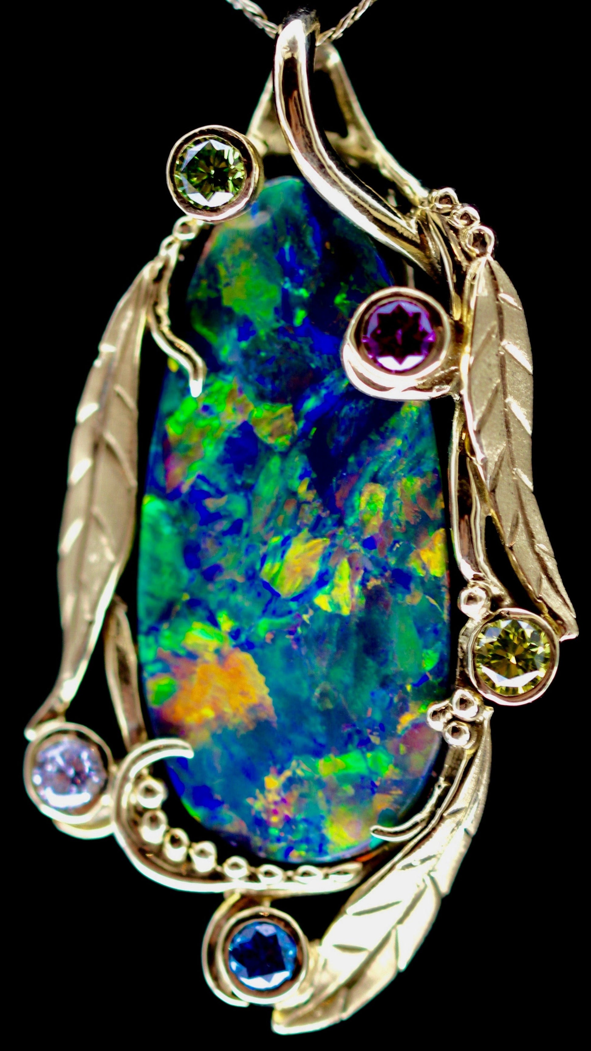 Straight-on macro of the black opal cabochon and leaf setting highlighting vivid play-of-colour.
