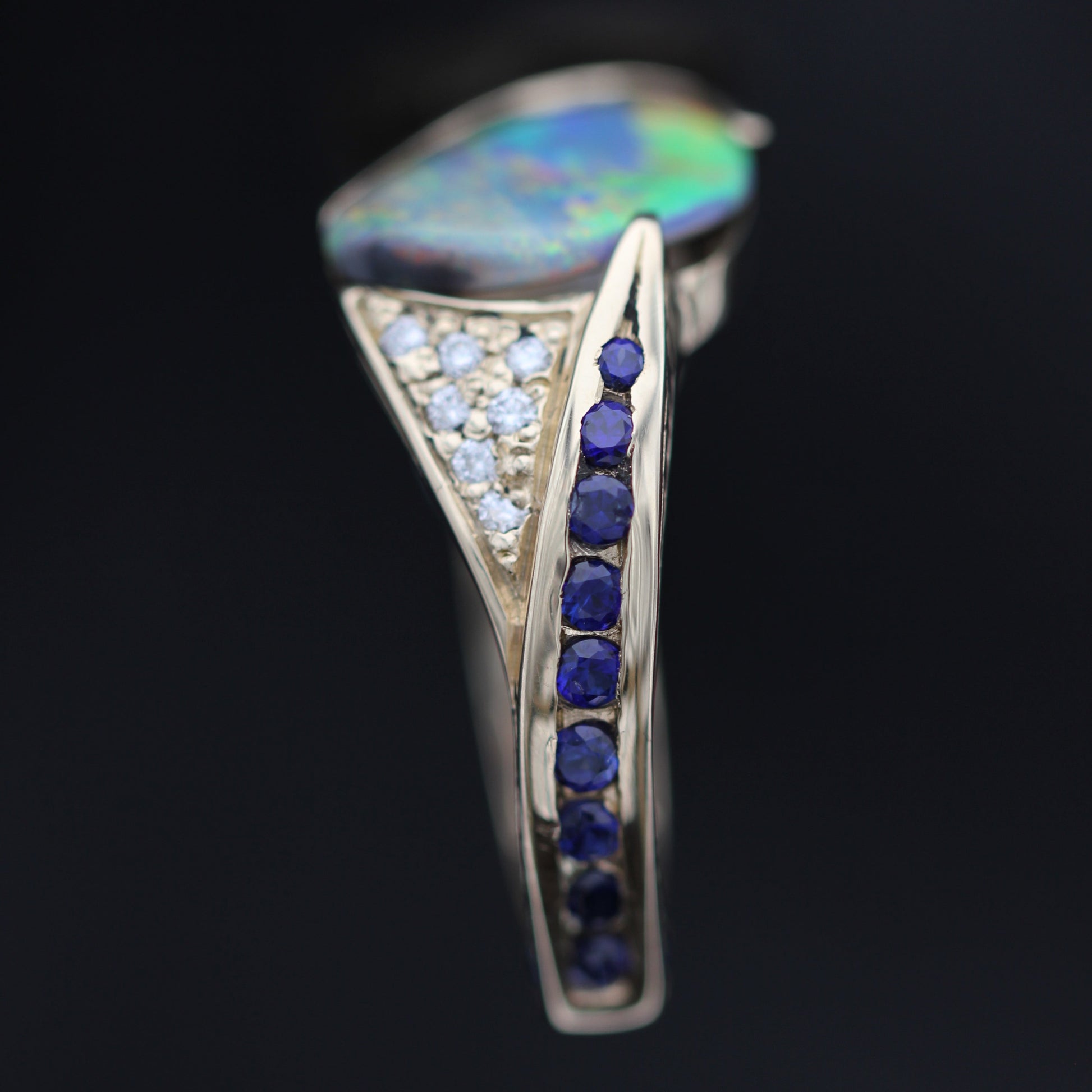 Macro detail of sapphire channel and diamond triangle on a Lightning Ridge black opal statement ring, 18ct yellow gold setting.