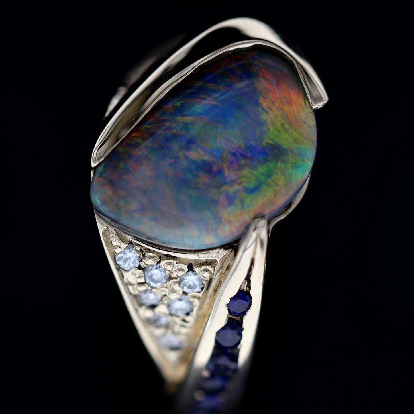 Close detail of blue sapphire accent row along the shank of a Lightning Ridge black opal ring in 18ct yellow gold.