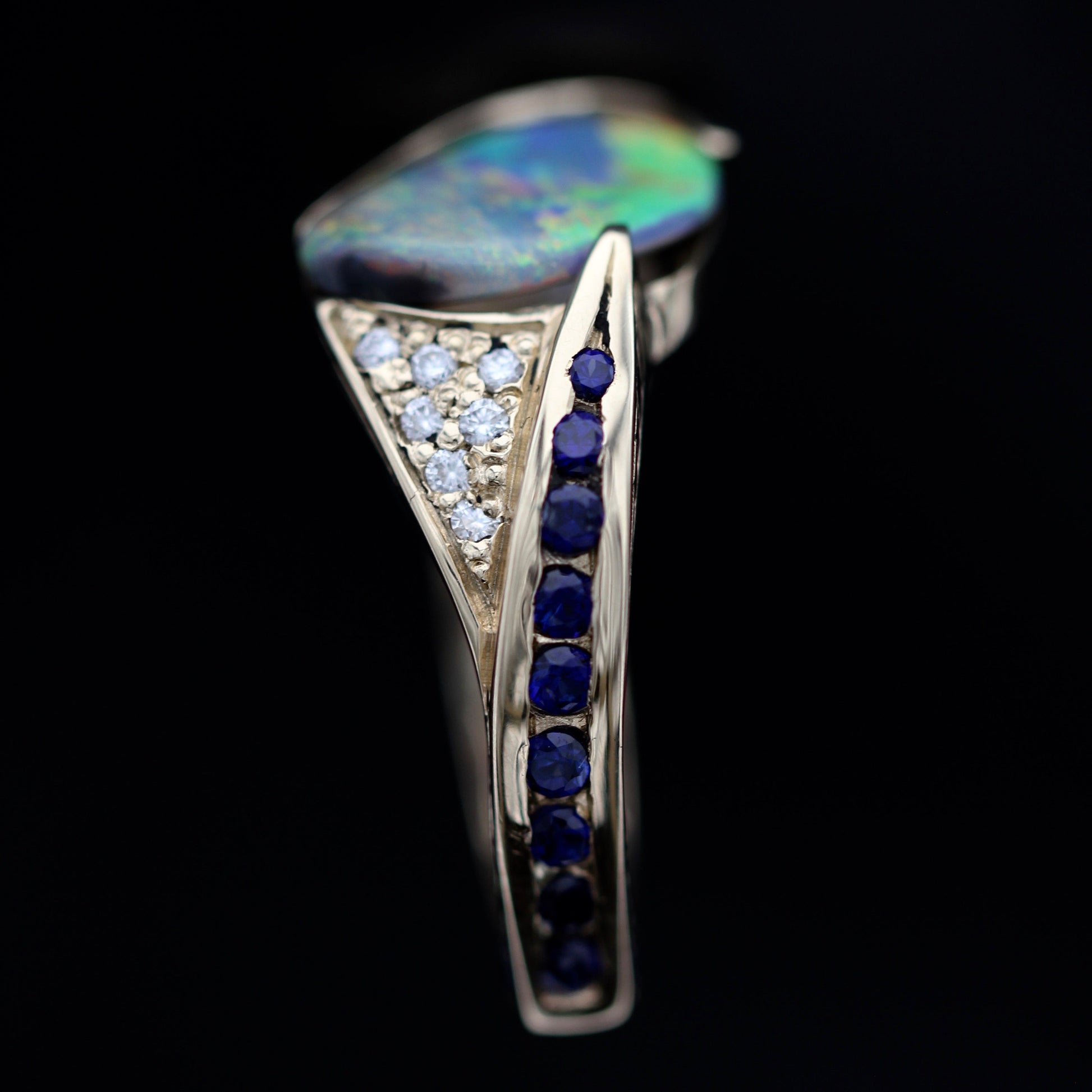Angled top view of 2.29ct Lightning Ridge black opal ring showing diamond pavé and sapphire accents in 18ct yellow gold.