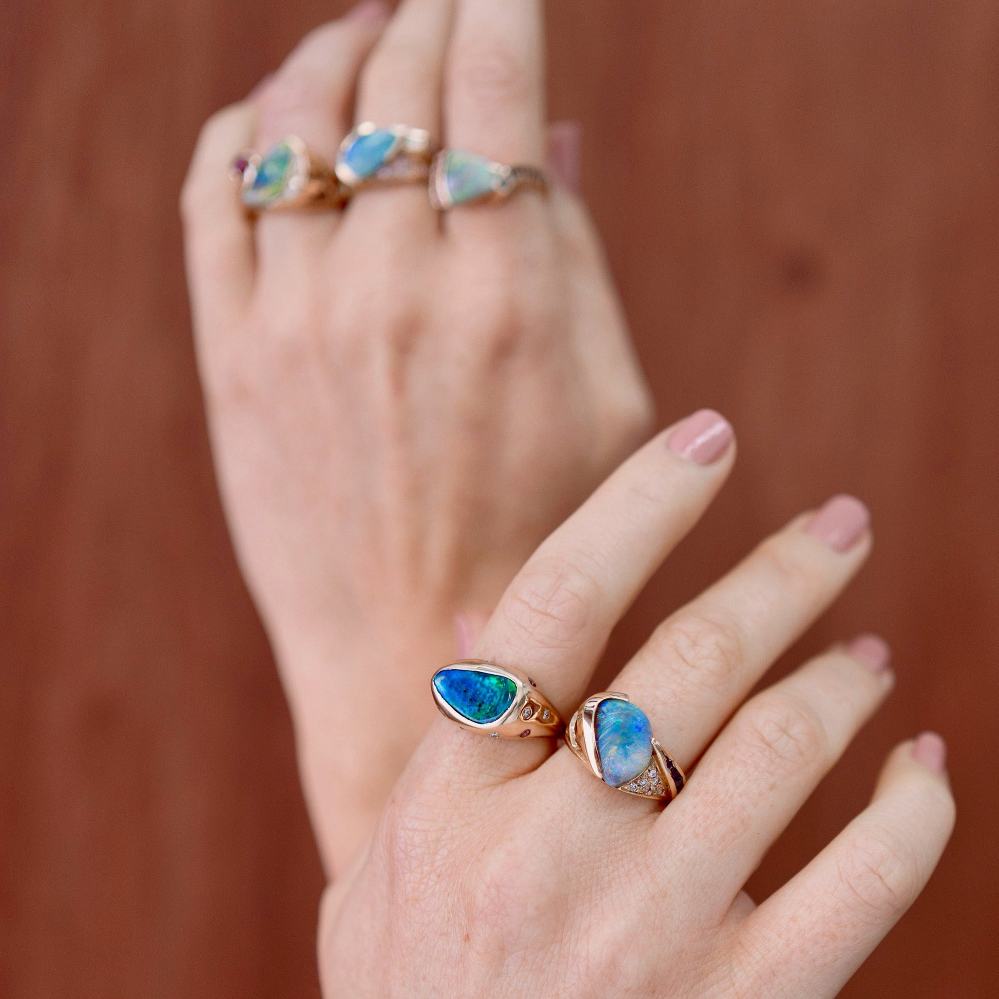 Lifestyle close-up of hands wearing a 2.29ct Lightning Ridge black opal ring with sapphire and diamond accents in 18ct yellow gold.