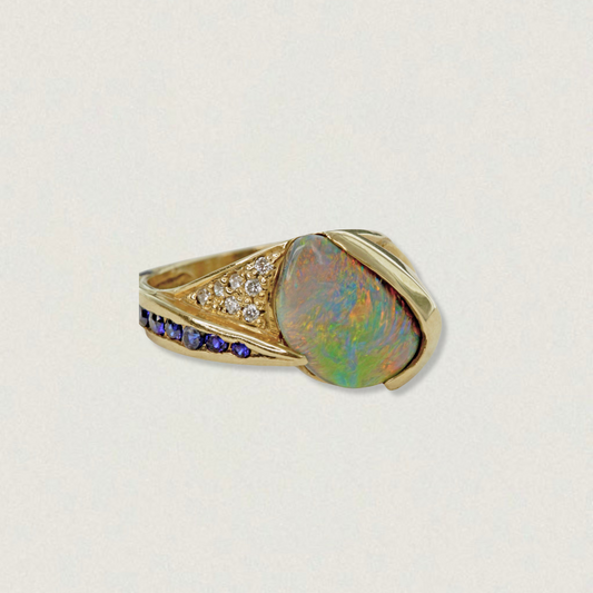 2.29ct Lightning Ridge black opal statement ring with blue sapphires and diamond accents in 18ct yellow gold, angled product view on light background.