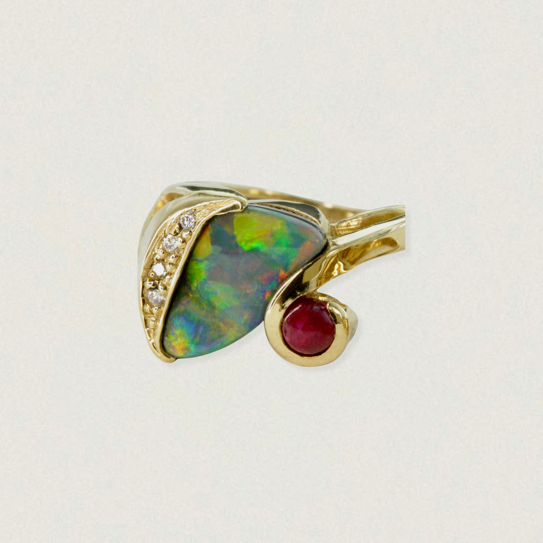 2.75ct Lightning Ridge black opal ring with diamond accents and ruby cabochon in 18ct yellow gold, product on light background.