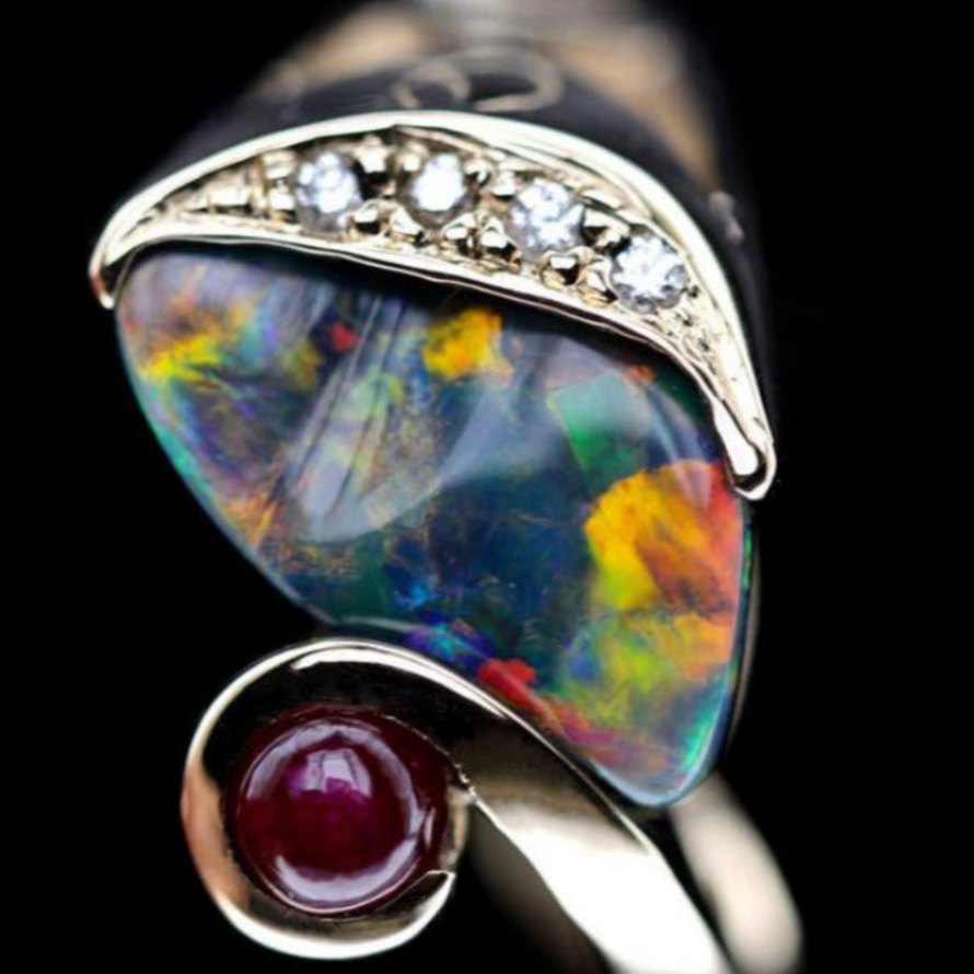 Macro of Lightning Ridge black opal with vivid play-of-colour, diamond pavé and ruby cabochon in yellow gold setting.