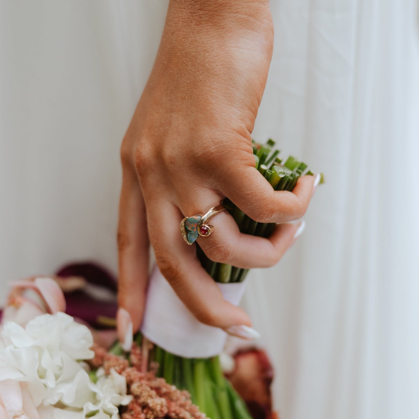 Bride holding bouquet wearing 2.75ct black opal, diamond and ruby ring in 18ct yellow gold.