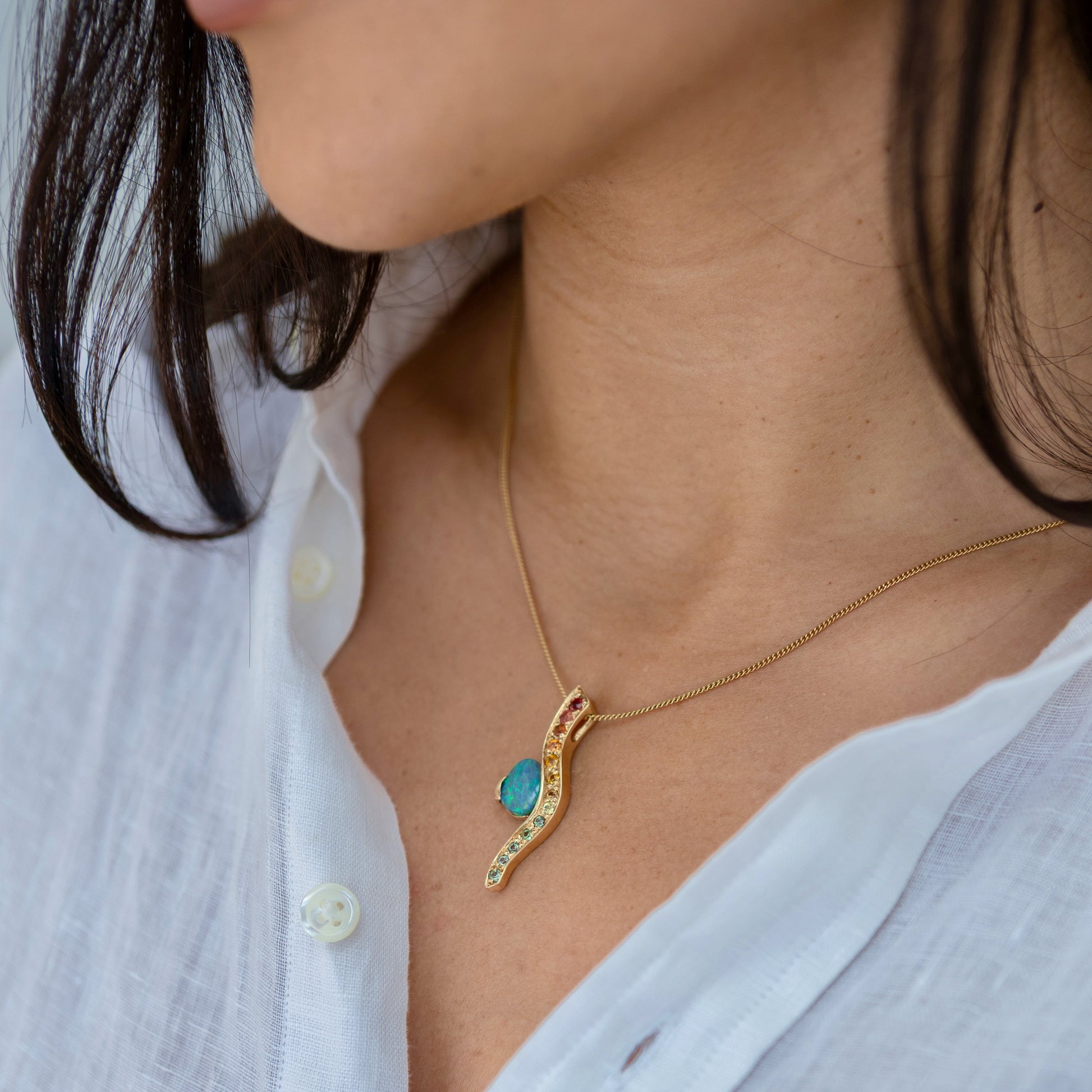 Pendant worn on a gold chain at the collarbone, showing the curved wave and vibrant opal.