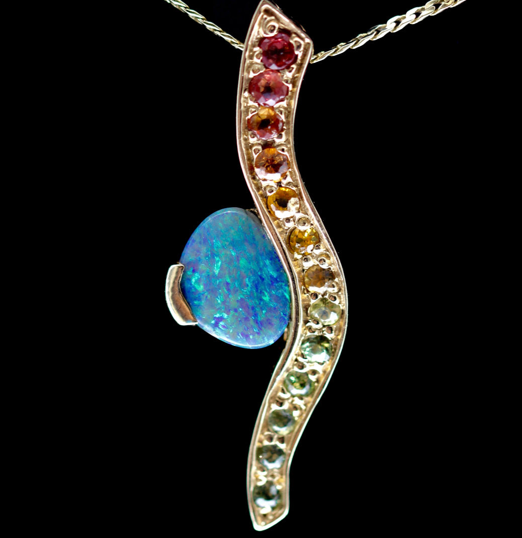 Front view on black background of the wave pendant with Lightning Ridge opal and sapphire gradient in 14ct yellow gold.