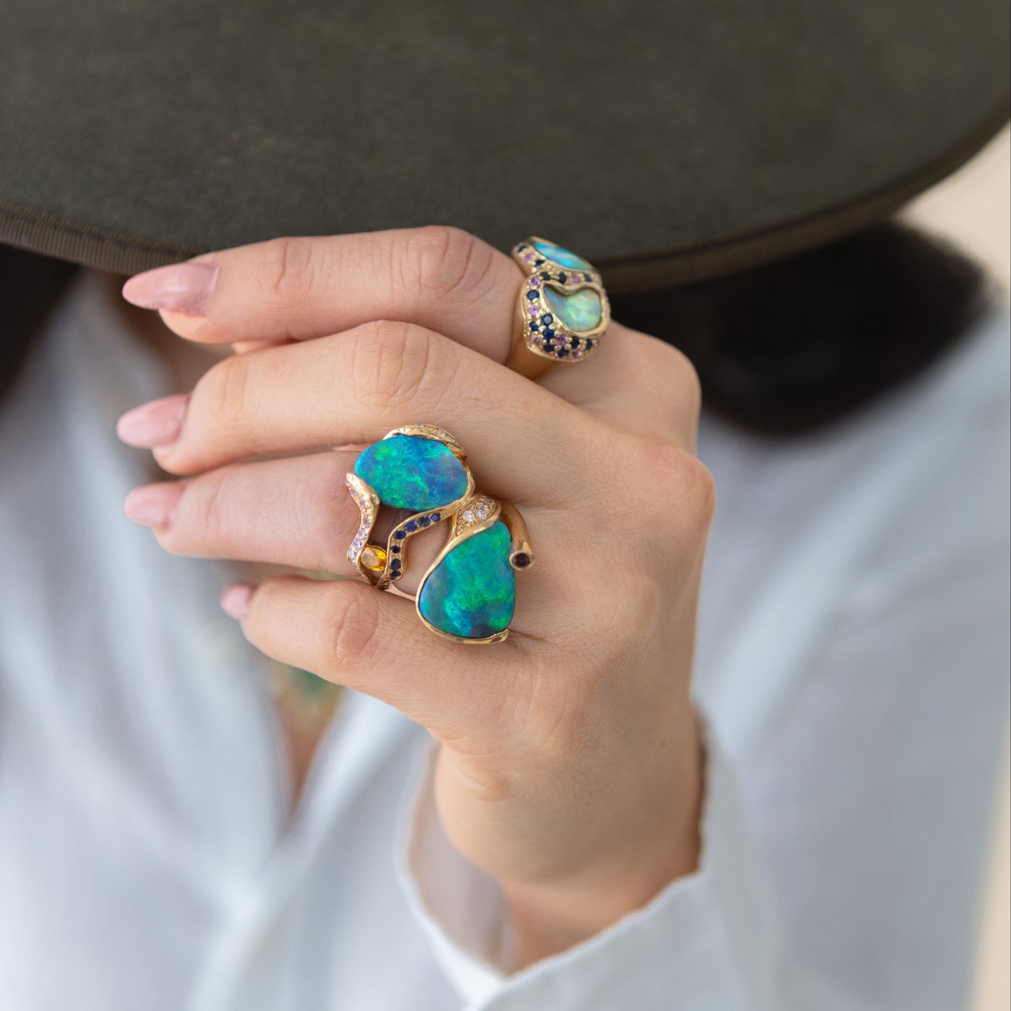 Styled hand shot showing the 5.85ct Lightning Ridge opal, sapphire and diamond cocktail ring in 18ct yellow gold worn on the index finger.