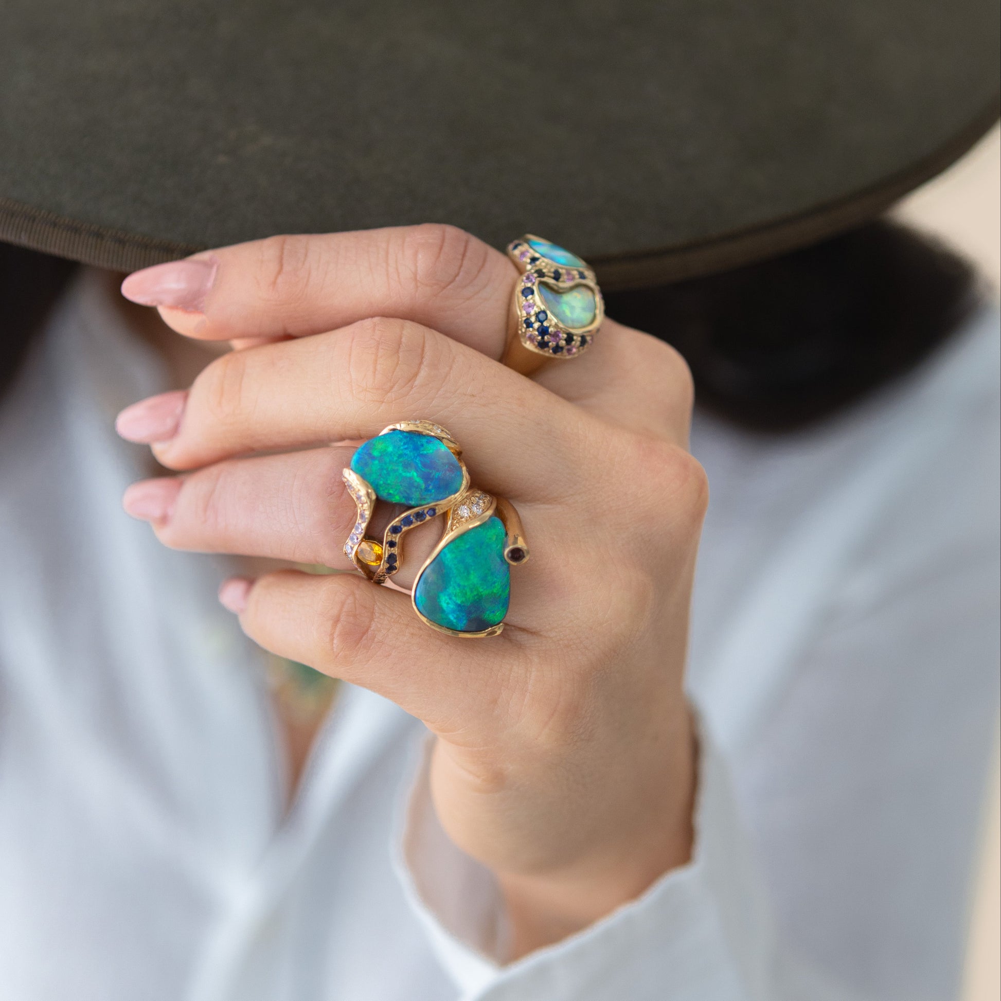 Styled hand shot showing the 5.85ct Lightning Ridge opal, sapphire and diamond cocktail ring in 18ct yellow gold worn on the index finger.