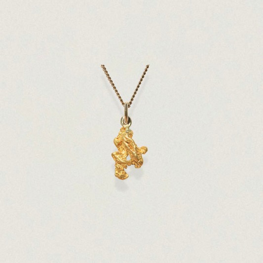 Natural gold nugget pendant in 18K with polished bail on neutral background
