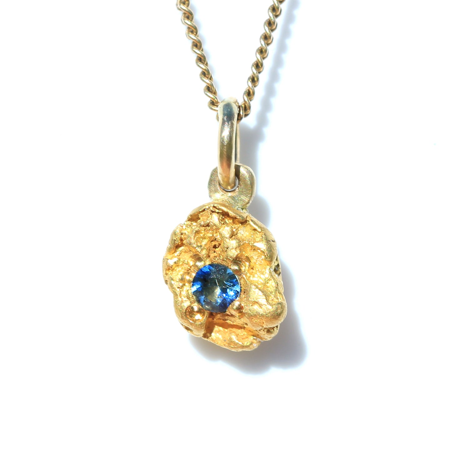 Close-up of natural Australian gold nugget pendant set with a round blue parti sapphire on chain, white background