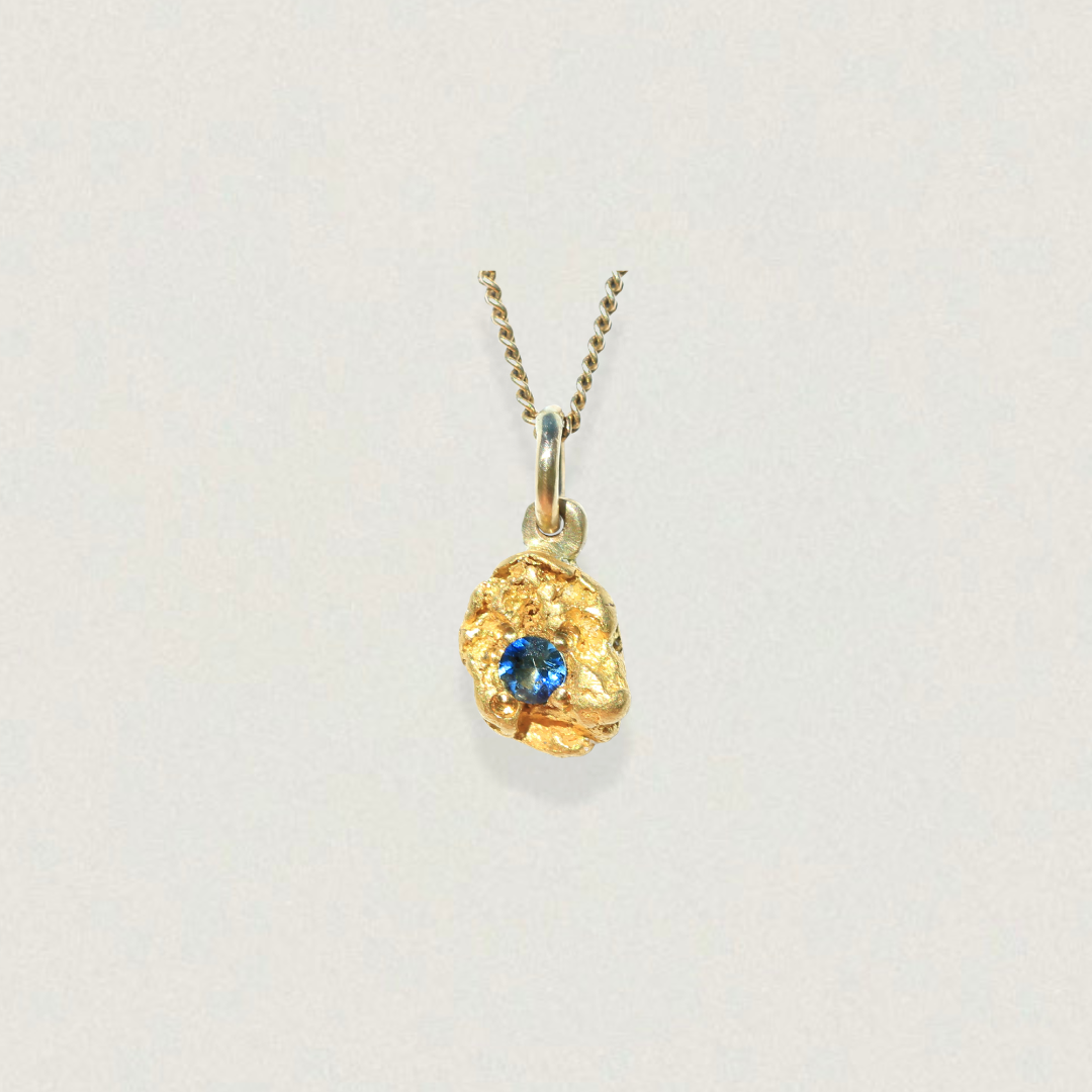 Australian natural gold nugget pendant set with a bright blue parti sapphire, front view on a light background.