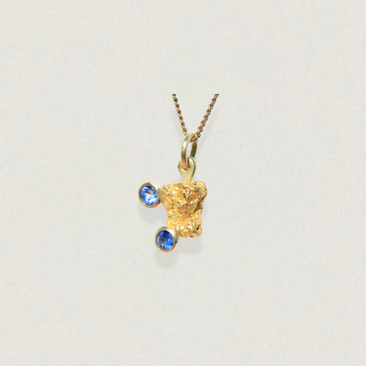 Australian natural gold nugget pendant set with two bright blue parti sapphires, front view on light background.