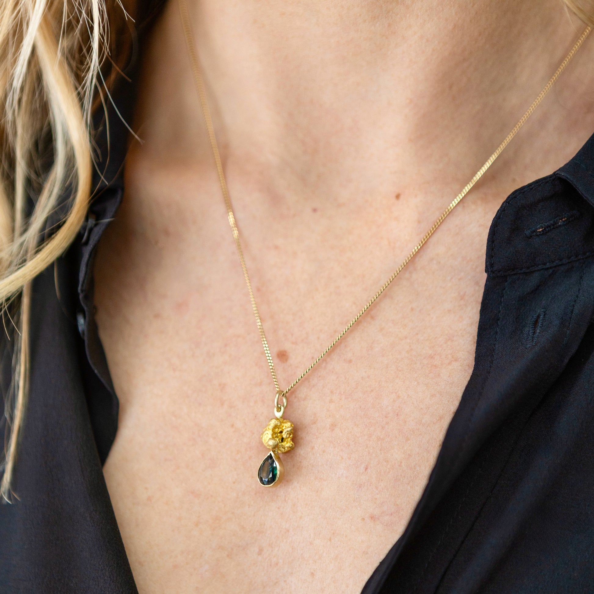 Woman wearing an Australian parti sapphire teardrop pendant set beneath a natural gold nugget on a fine gold chain (close-up neckline).