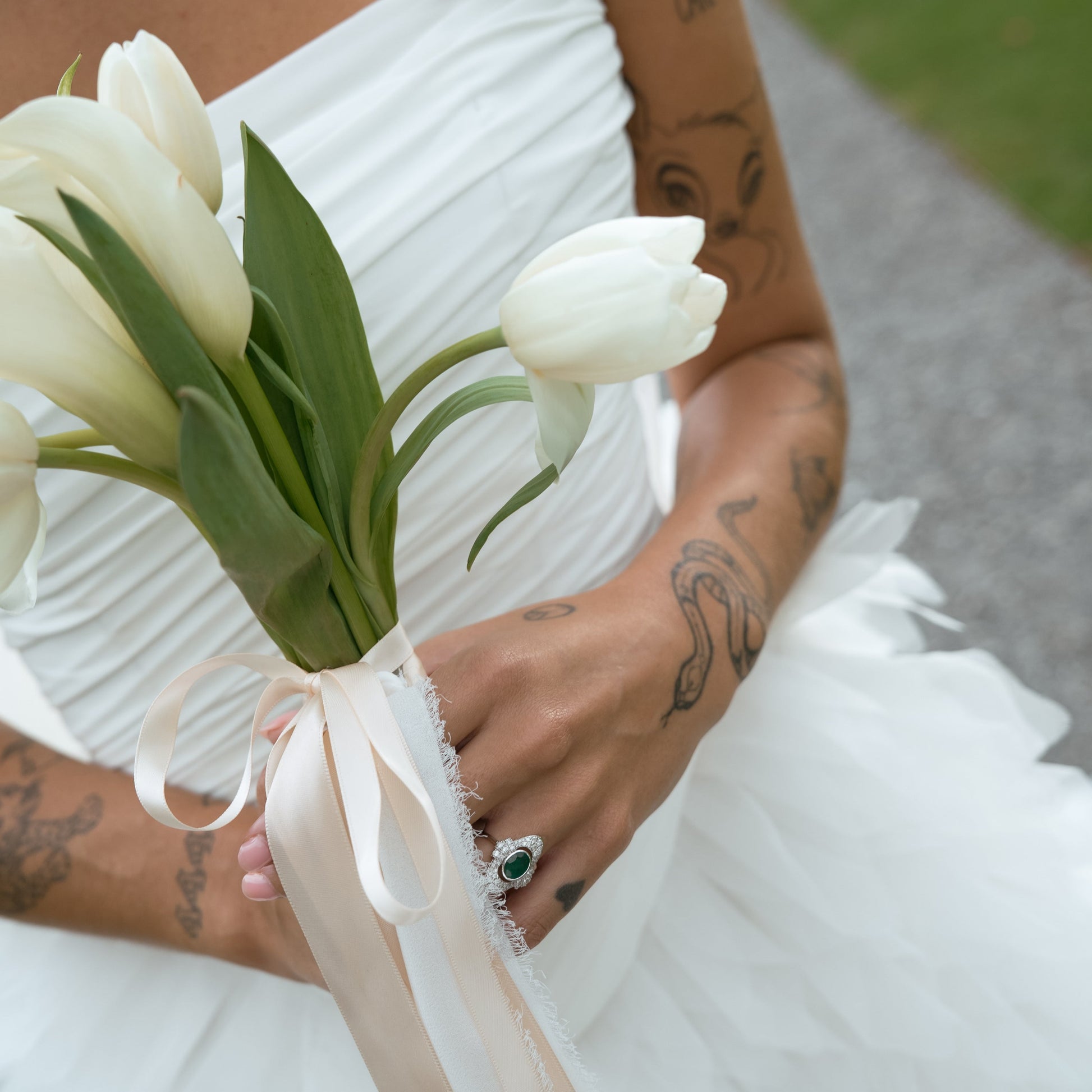 Close view of emerald and diamond Art Deco ring on bride’s hand holding a bouquet.