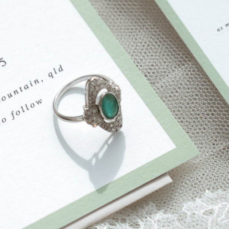 Art Deco emerald and diamond engagement ring in white gold styled on wedding invitation flat lay.
