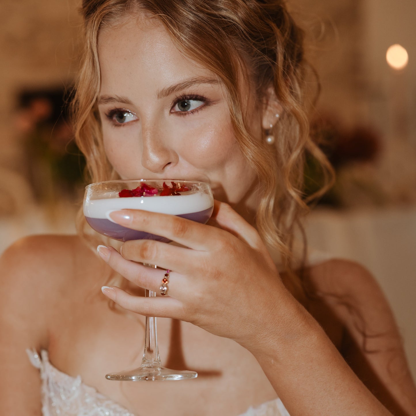 Lifestyle image of a woman holding a cocktail while wearing the five-stone colour-change zircon engagement ring with garnet and pink sapphire.