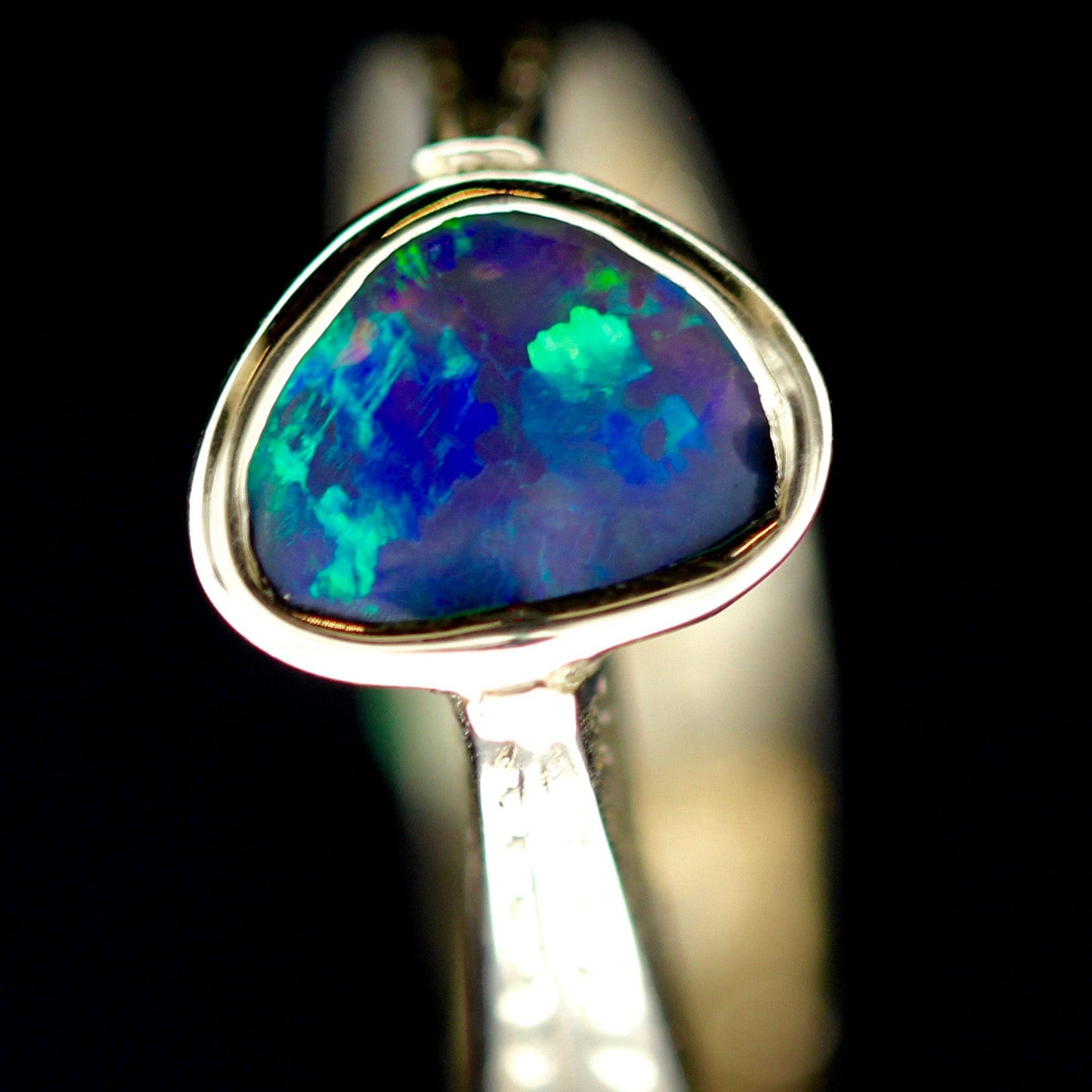 Close-up of bezel-set Lightning Ridge black opal showing blue-green play-of-colour in 14k yellow gold.