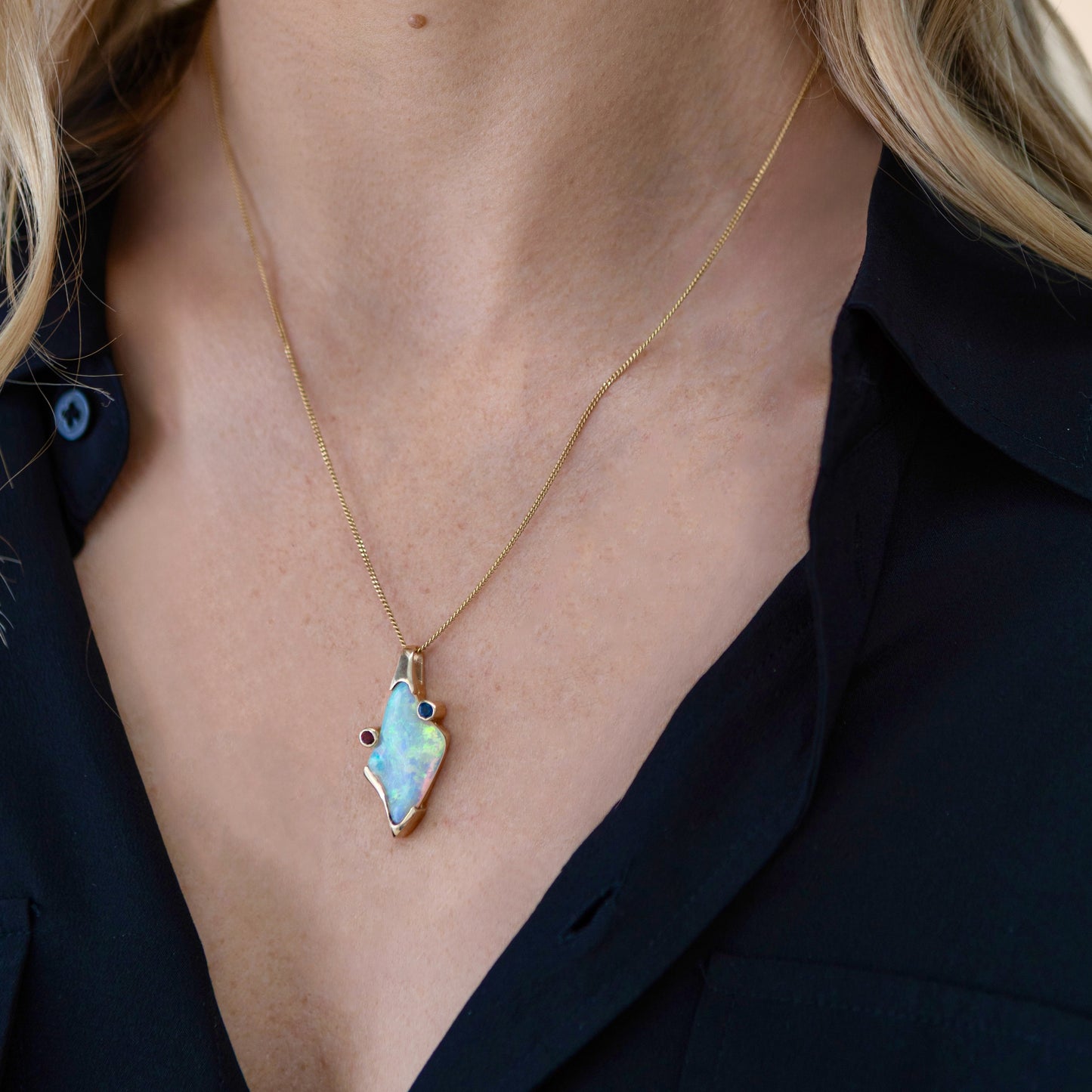Model wearing a Lightning Ridge crystal opal pendant with orange and blue sapphire accents on a fine chain