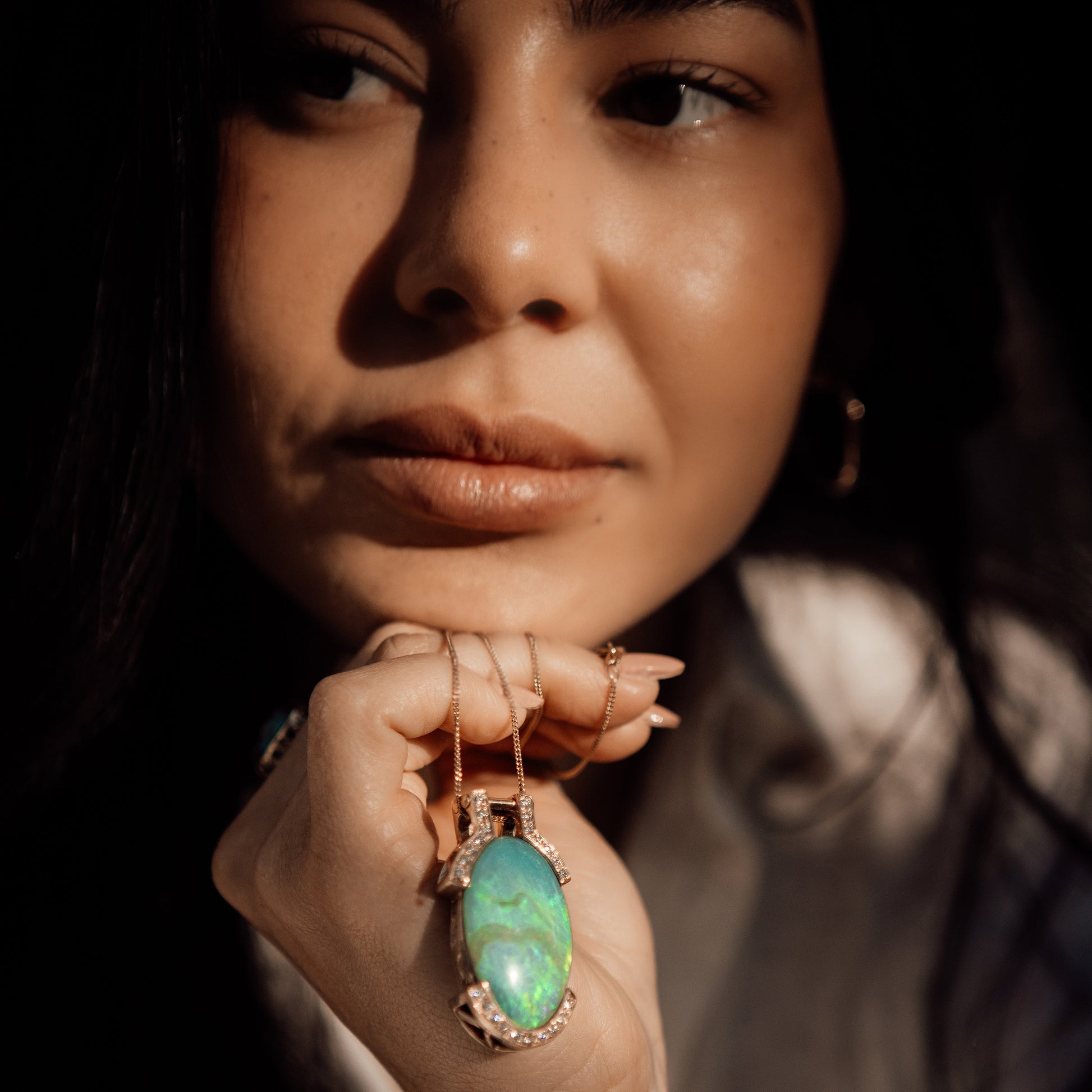 Model holding an oval Lightning Ridge opal and diamond pendant in 18ct yellow gold, showing size and colour play