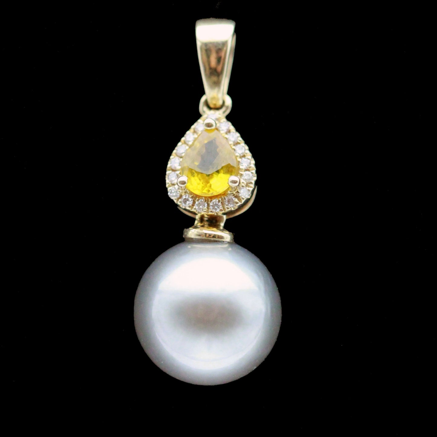 Close-up of pear-cut yellow sapphire with diamond halo and lustrous grey Tahitian pearl pendant, 14ct yellow gold.