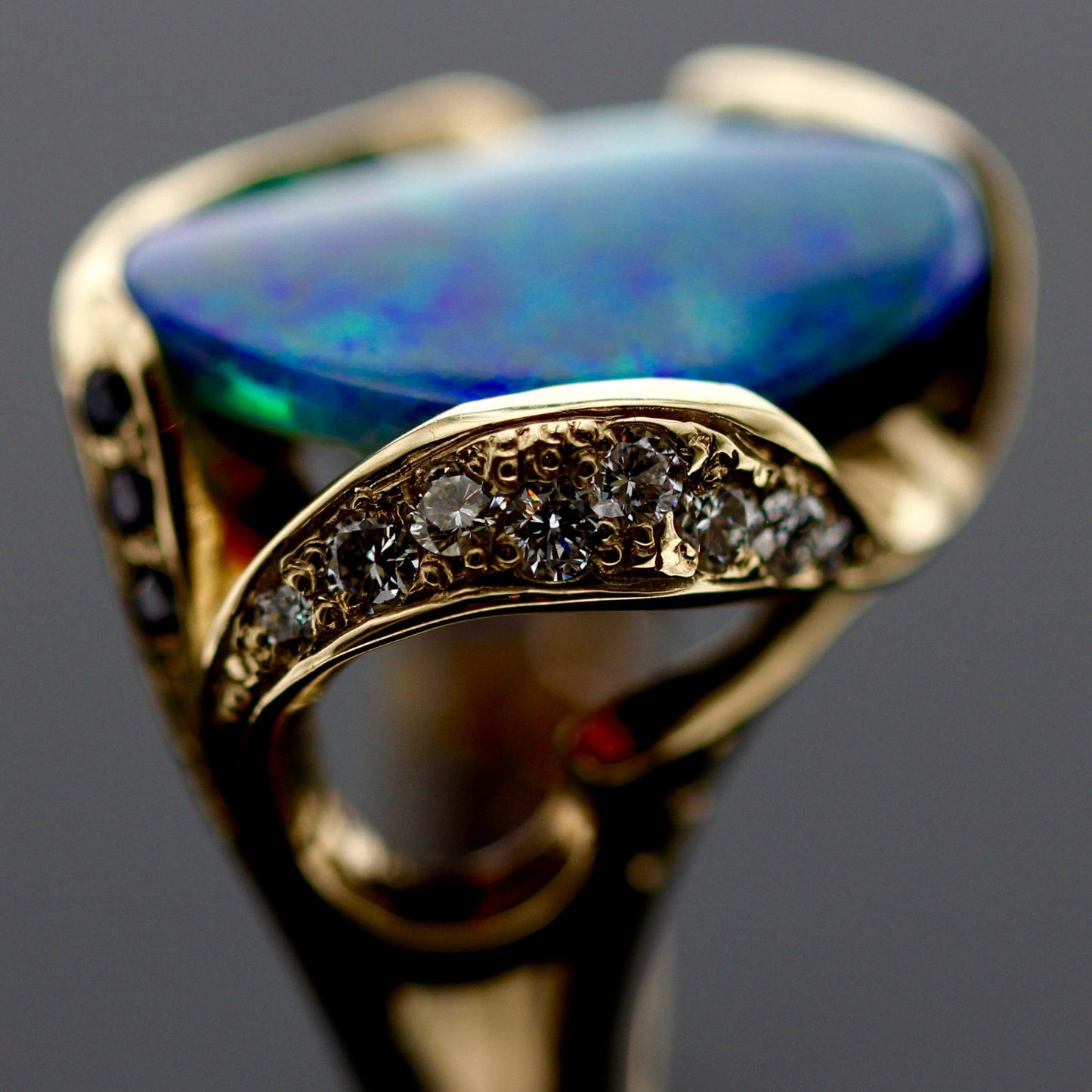 Angled profile showing sapphire pavé and raised setting of the 5.85ct Lightning Ridge opal ring in 18ct yellow gold.